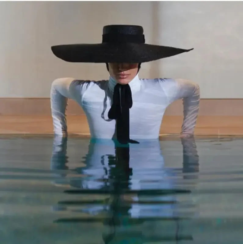 Woman wearing black wind brim hat and black tie in water with reflection