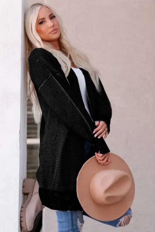 Blonde woman wearing Fashionsarah gray and white duster cardigan holding a hat