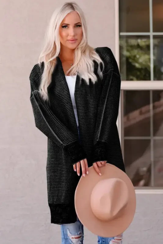 Woman in fashionsarah gray and white duster cardigan holding a hat, showcasing knit pocketed design