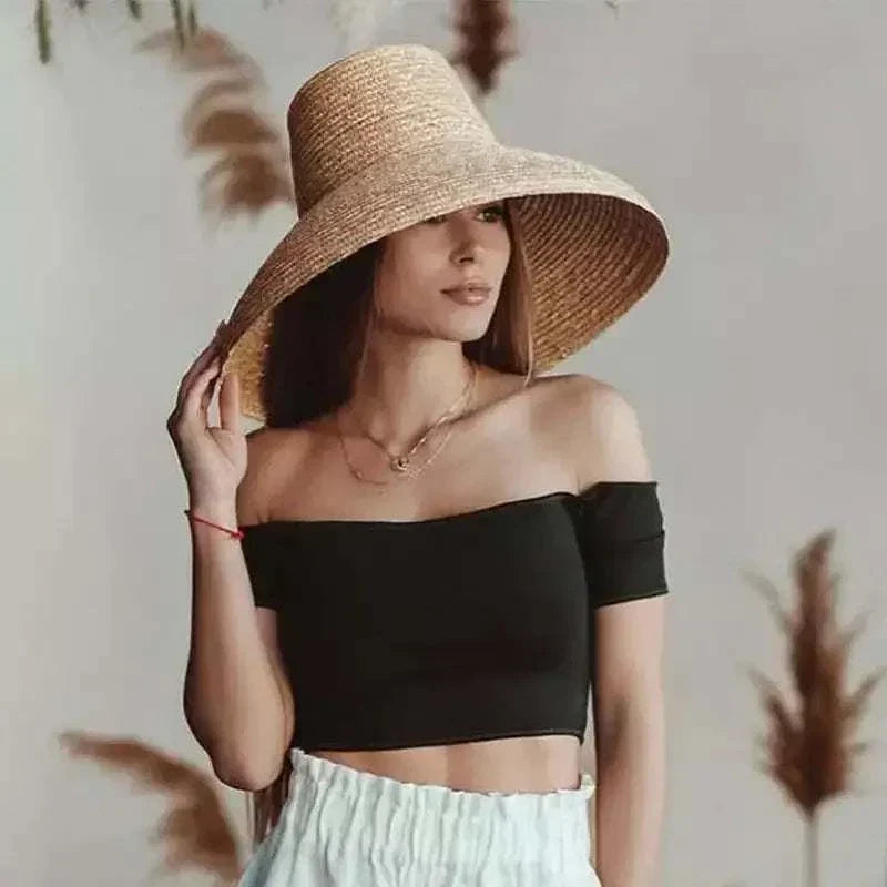 Woman wearing a solid straw sun hat with wide brim and navy band, styled with off-shoulder black top and white skirt