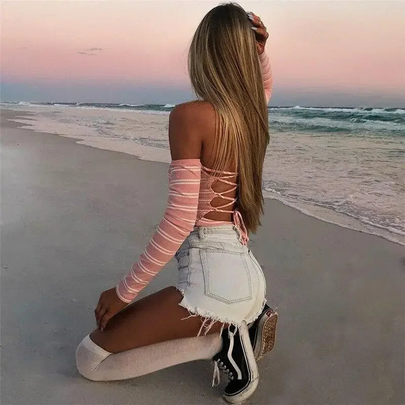 Kneeling woman in pink backless bodysuit with denim shorts, stylish backless outfit