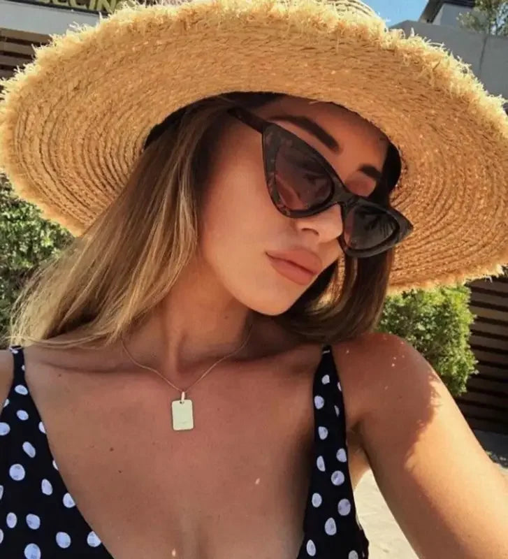Woman with vintage cat sunglasses, straw hat, and scarf outdoors for stylish elegance