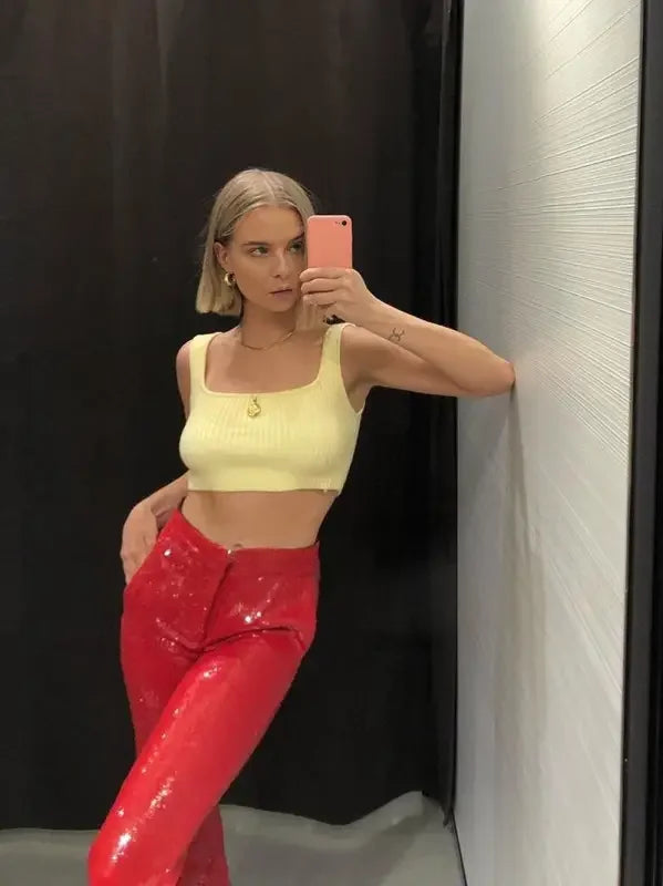Woman in yellow crop top and red pants taking a selfie, showcasing fashion sequin blazer and trousers